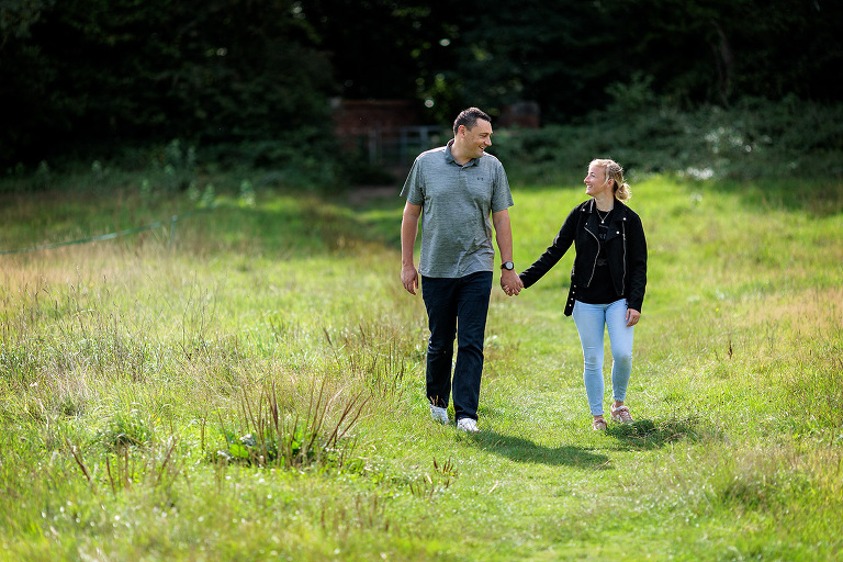 engaged couple walking in field at Winchfield
